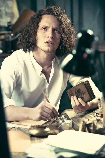 Écrivain au travail. Beau jeune écrivain assis à la table et écrit quelque chose dans son carnet de croquis