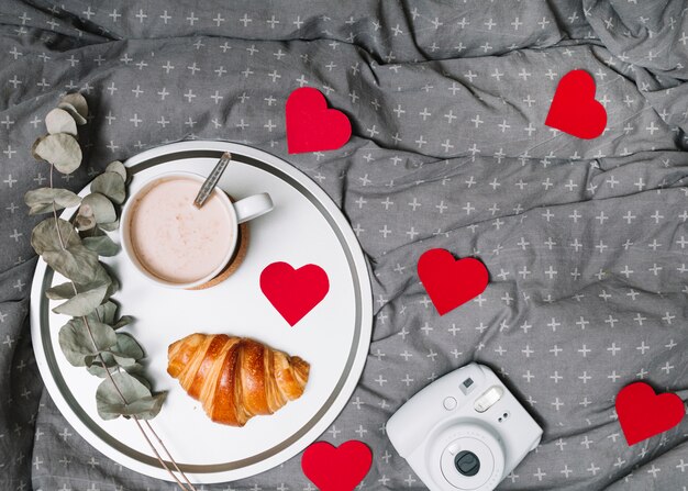 Croissant, brindille et tasse de boisson sur un plateau près de coeurs d&#39;ornement et caméra