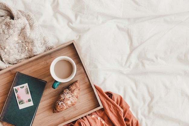 Croissant et café près du livre sur le lit