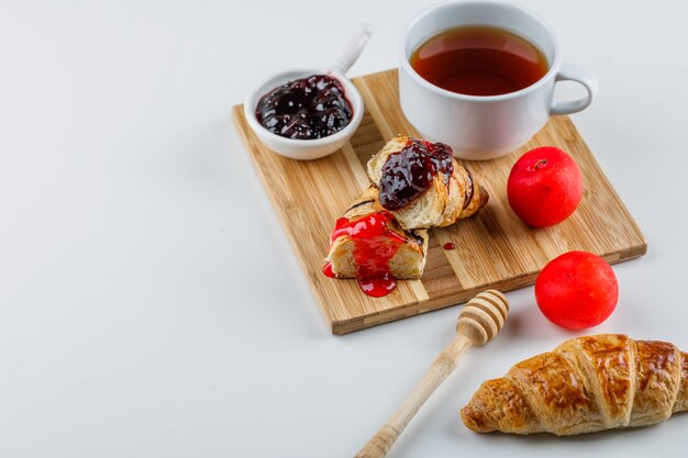 Croissant avec confiture, prunes, louche, thé high angle view on white et planche à découper