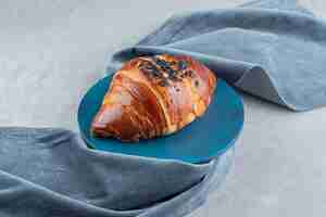 Photo gratuite croissant frais décoré de goutte de chocolat sur planche bleue.