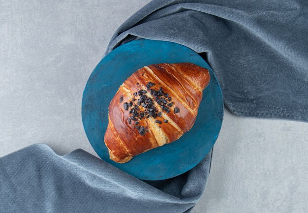 Croissant frais décoré de goutte de chocolat sur planche bleue.