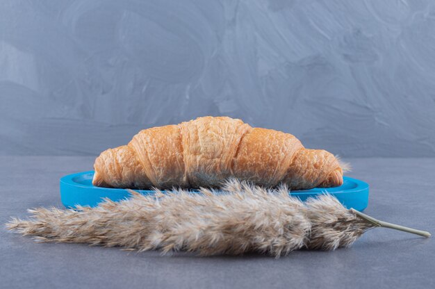 Croissant français fraîchement sorti du four sur planche de bois bleue.