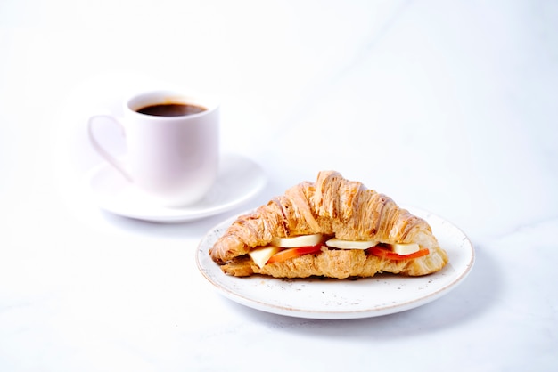 Croissant garni de fromage et tomate et une tasse de café