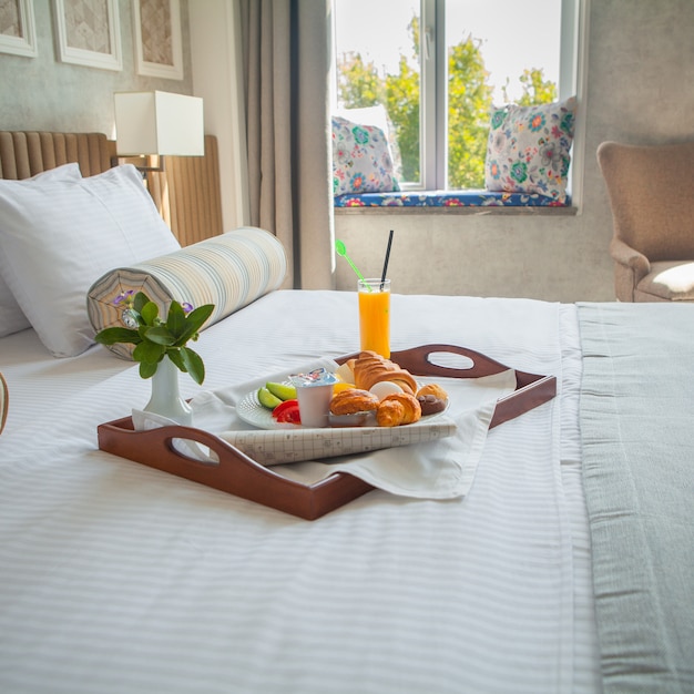 Croissant, œuf à la coque, jus d'orange, petit déjeuner au yaourt sur plateau au lit dans la chambre d'hôtel