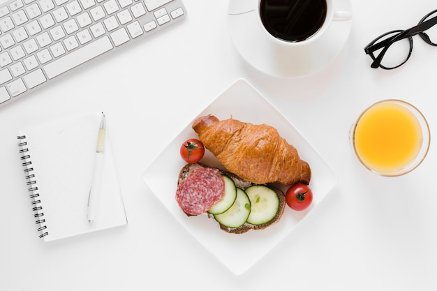 Photo gratuite croissant et sandwich sur assiette avec jus d'orange café et cahier