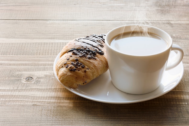 Des croissants au chocolat fraîchement sortis du four et une tasse de café sur une planche de bois. concept de petit déjeuner.