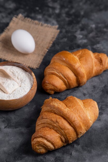 Croissants fraîchement sortis du four avec des œufs de poule et bol de farine en bois.