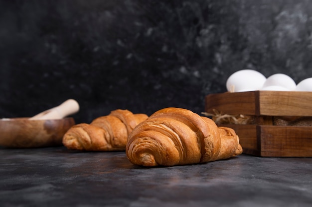 Croissants fraîchement sortis du four avec des œufs de poule et bol de farine en bois.