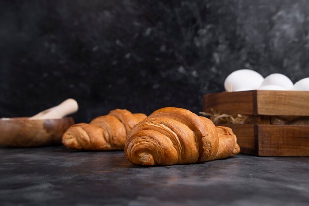 Croissants fraîchement sortis du four avec des œufs de poule et bol de farine en bois.