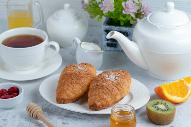 Croissants frais avec une tasse de thé et des fruits sucrés.