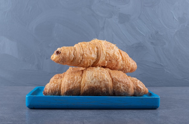 Croissants français frais avec une croûte dorée. Sur une planche de bois bleue.