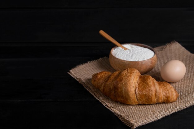 Croissants nature, bol de farine et œufs crus sur une surface en bois sombre. Photo de haute qualité