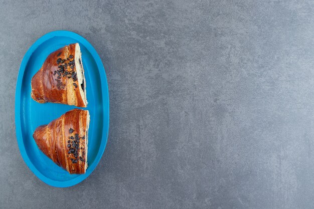 Croissants savoureux à moitié coupés au chocolat sur plaque bleue.