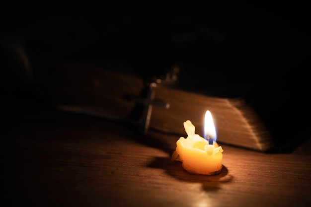 Croix avec bible et bougie sur une vieille table en bois de chêne.