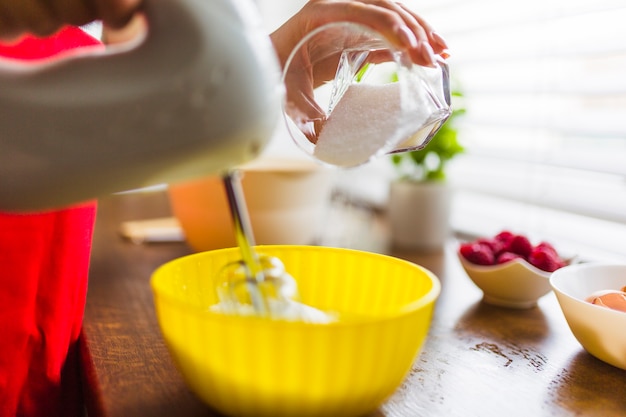 Crop femme ajoutant du sucre dans la crème fouettée