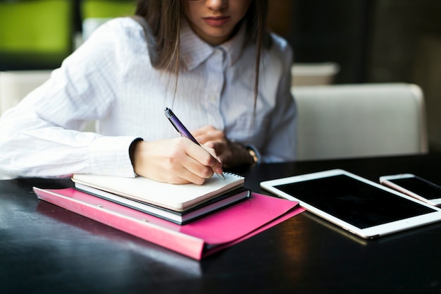 Crop femme prenant des notes au café