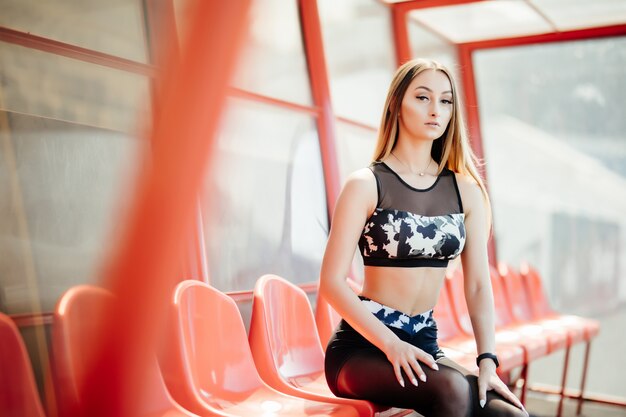 Crop fit femelle en tenue sportive moderne assis sur une chaise colorée du stade tribune se préparer pour la formation