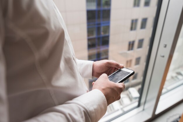 Crop homme d&#39;affaires à l&#39;aide de smartphone à la fenêtre