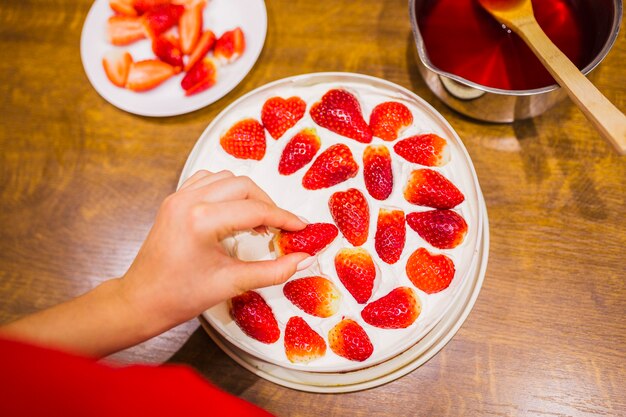Crop main décorer le gâteau avec des fraises