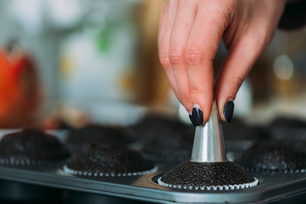 Crop main découpant des cavités dans des cupcakes