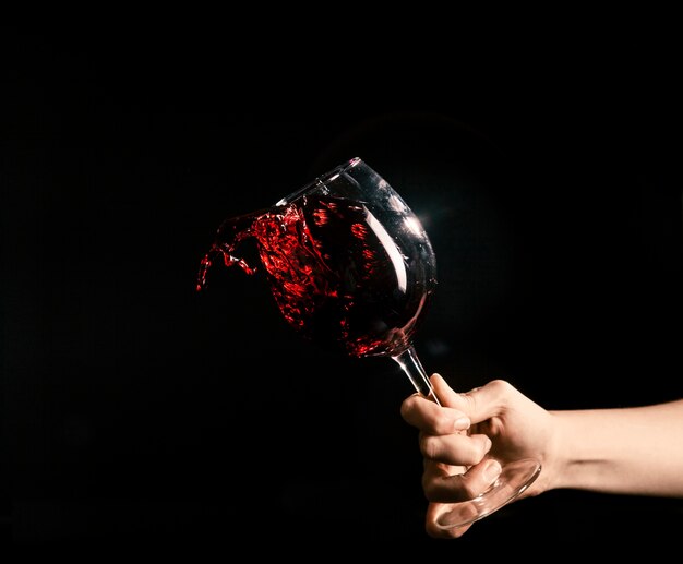 Crop main éclaboussant le vin du verre