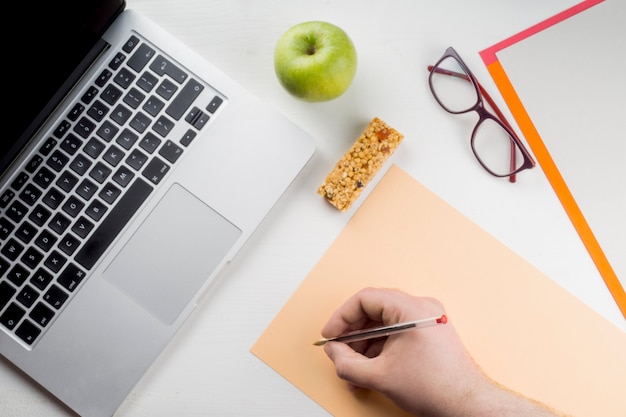 Crop main écrivant près d&#39;ordinateur portable et apple