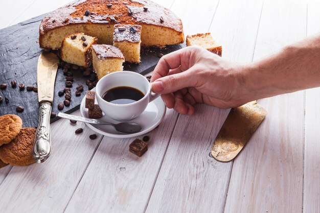 Crop main prenant le café près du gâteau