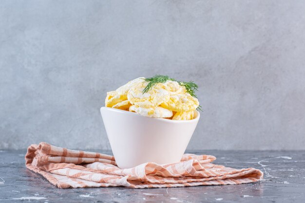 Croustilles au fromage dans un bol sur un torchon, sur la surface en marbre