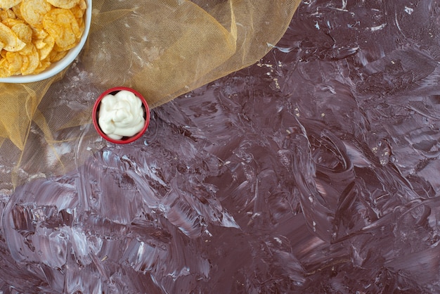 Croustilles croustillantes et yaourt dans une assiette sur tulle, sur la table en marbre.