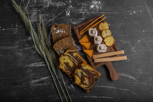 Croustilles avec des produits de pâtisserie sur un plateau en bois et tranches de pain de côté, vue du dessus