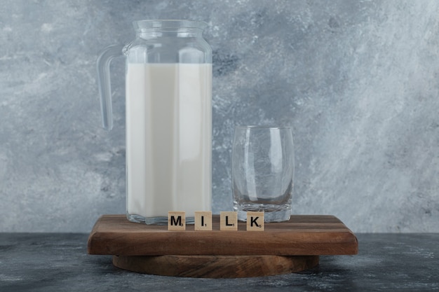 Photo gratuite cruche de lait et verre d'eau sur planche de bois.