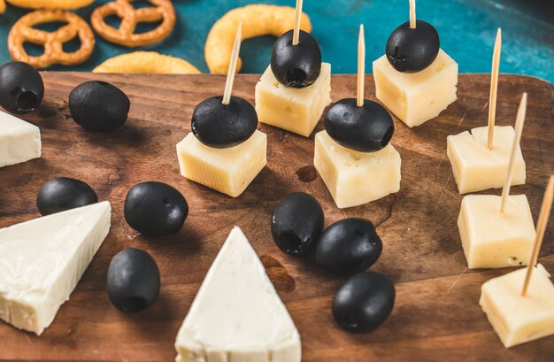 Cubes de fromage et olives noires sur une planche de bois avec des craquelins