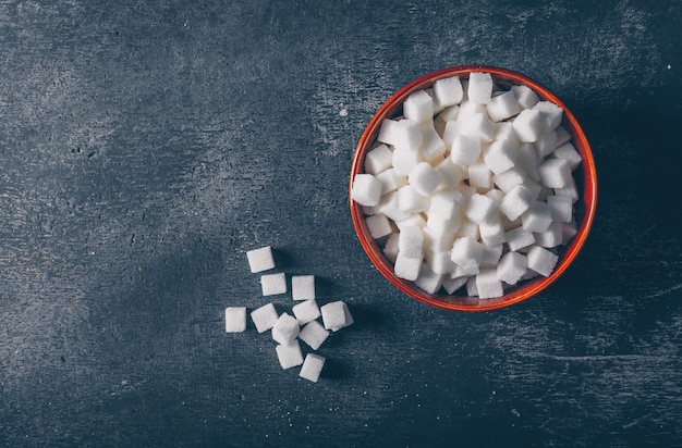 Photo gratuite cubes de sucre blanc dans un bol sur fond texturé foncé, vue de dessus. espace pour le texte