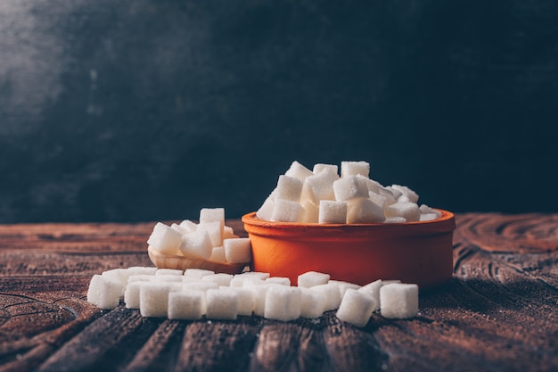 Photo gratuite cubes de sucre blanc dans un bol orange avec vue latérale cuillère sur une table sombre et en bois