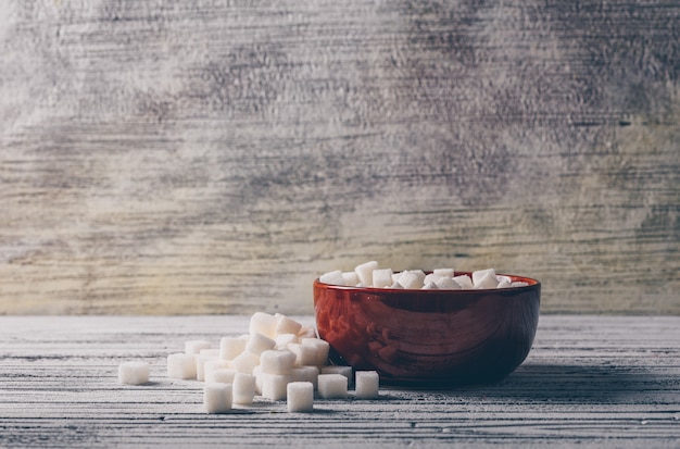 Cubes de sucre blanc dans un bol sur une table en bois blanc. vue de côté.