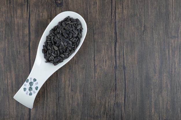 Cuillère blanche pleine de graines de tournesol noires saines placées sur une table en bois.