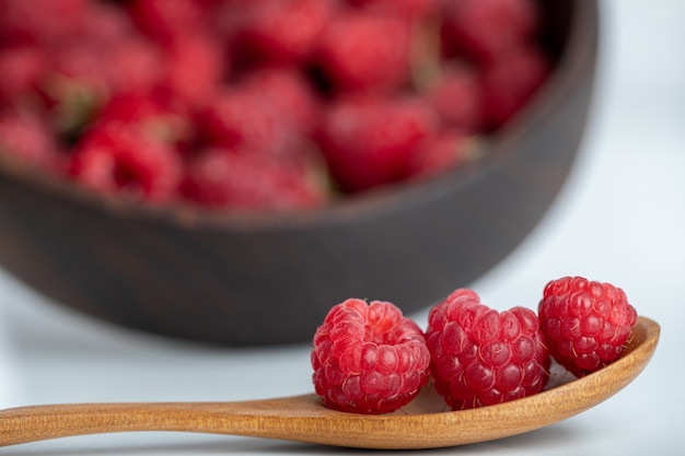 cuillère en bois de framboises mûres saines placées sur une table en pierre