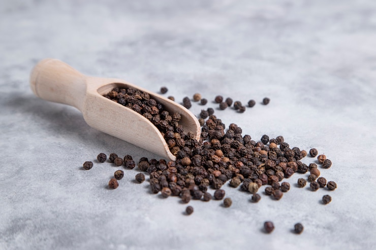 Photo gratuit une cuillère en bois pleine de grains de poivre noir placés sur une table en pierre. photo de haute qualité
