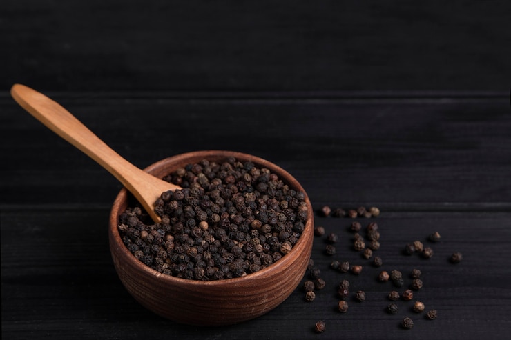 Photo gratuit une cuillère en bois pleine de grains de poivre posée sur une table en bois sombre. photo de haute qualité
