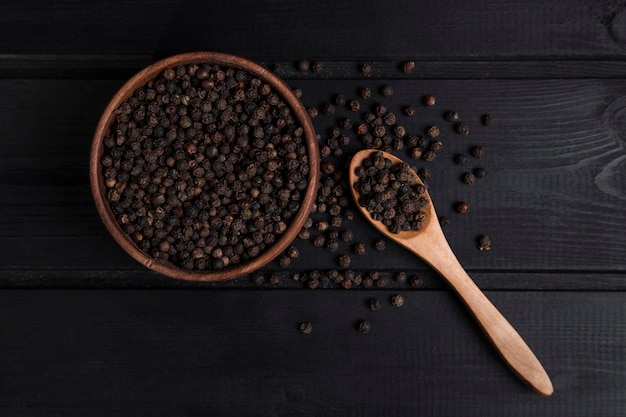 Une cuillère en bois pleine de grains de poivre posée sur une table en bois sombre. Photo de haute qualité