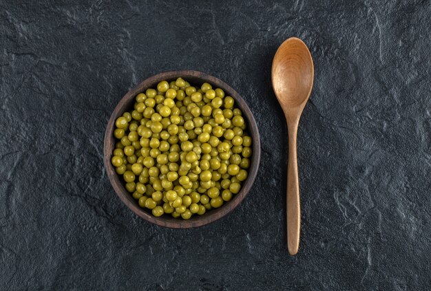 Cuillère et bol en bois remplis de petits pois verts marinés.