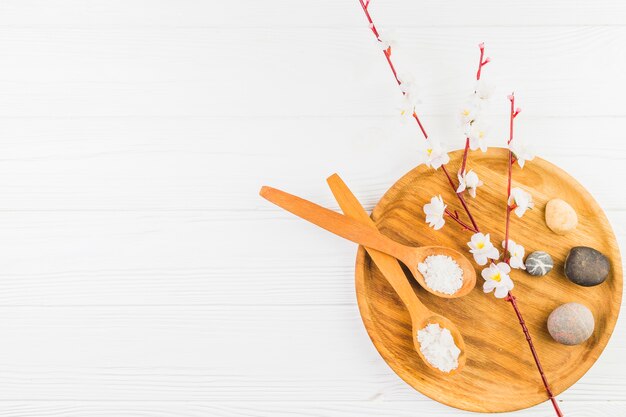 Cuillère à sel; fleurs et pierre spa sur planche de bois sur une surface blanche