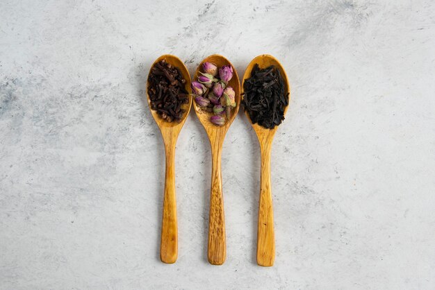 Cuillères en bois avec roses séchées, thés en vrac et clous de girofle.