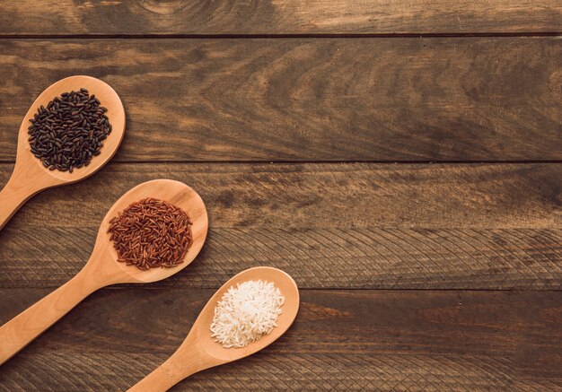 Cuillères en bois avec trois types différents de grains de riz sur une planche de bois