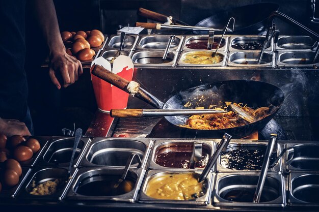 Le cuisinier fait frire des légumes avec des épices et de la sauce dans un wok. Processus de cuisson dans un restaurant asiatique.