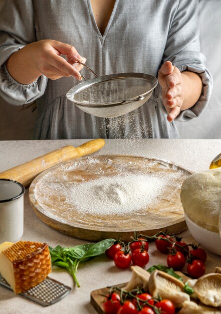 Cuisinier femme tamisant la farine sur planche de bois pour rouler la pâte à pizza