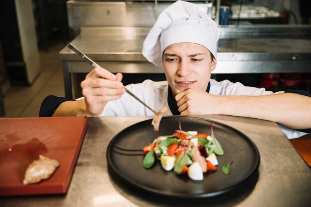 Cuisinier préparant une salade avec de la viande frite à table