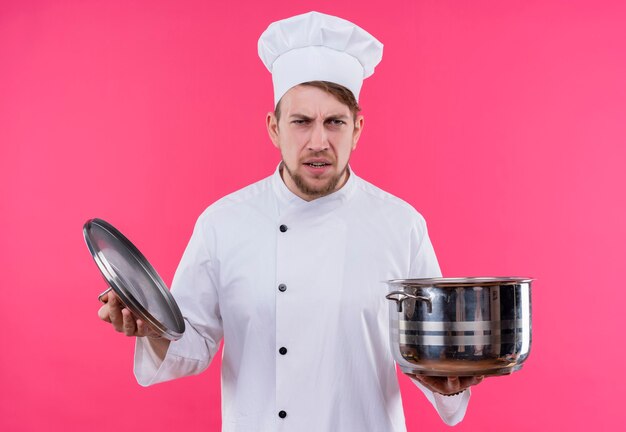 Cuisinier regardant la caméra en colère sur le visage avec une casserole sur place debout sur un mur rose