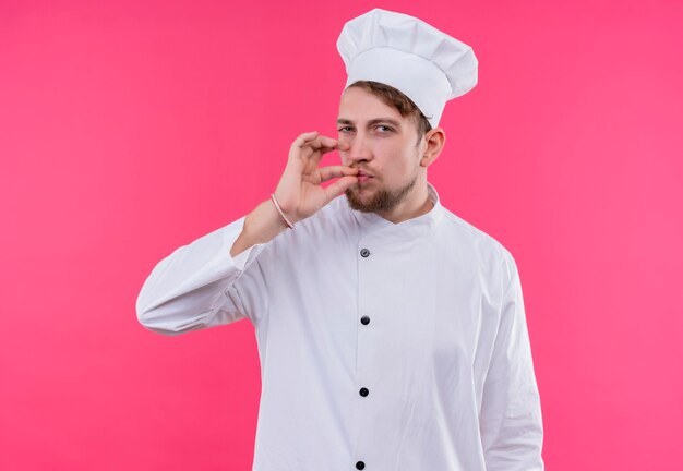 Cuisinier regardant la caméra faisant un geste délicieux debout sur un mur rose